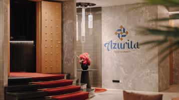 Un vestíbulo con alfombra roja, una recepción y una pared con el nombre 'Azurita Restaurant' en una tipografía estilizada.