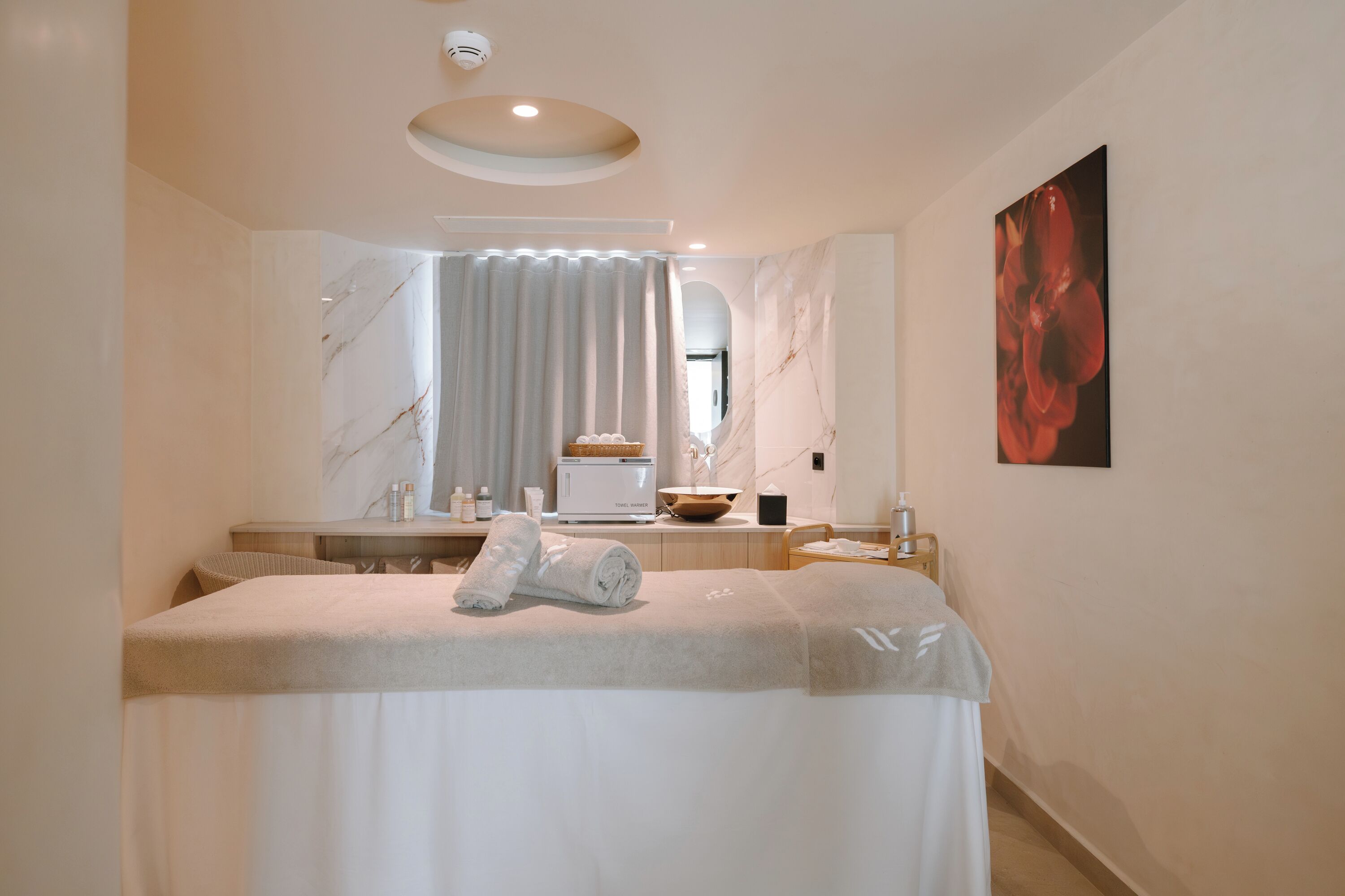 A modern spa room with a massage table, a large mirror, a marble wall, and a painting.