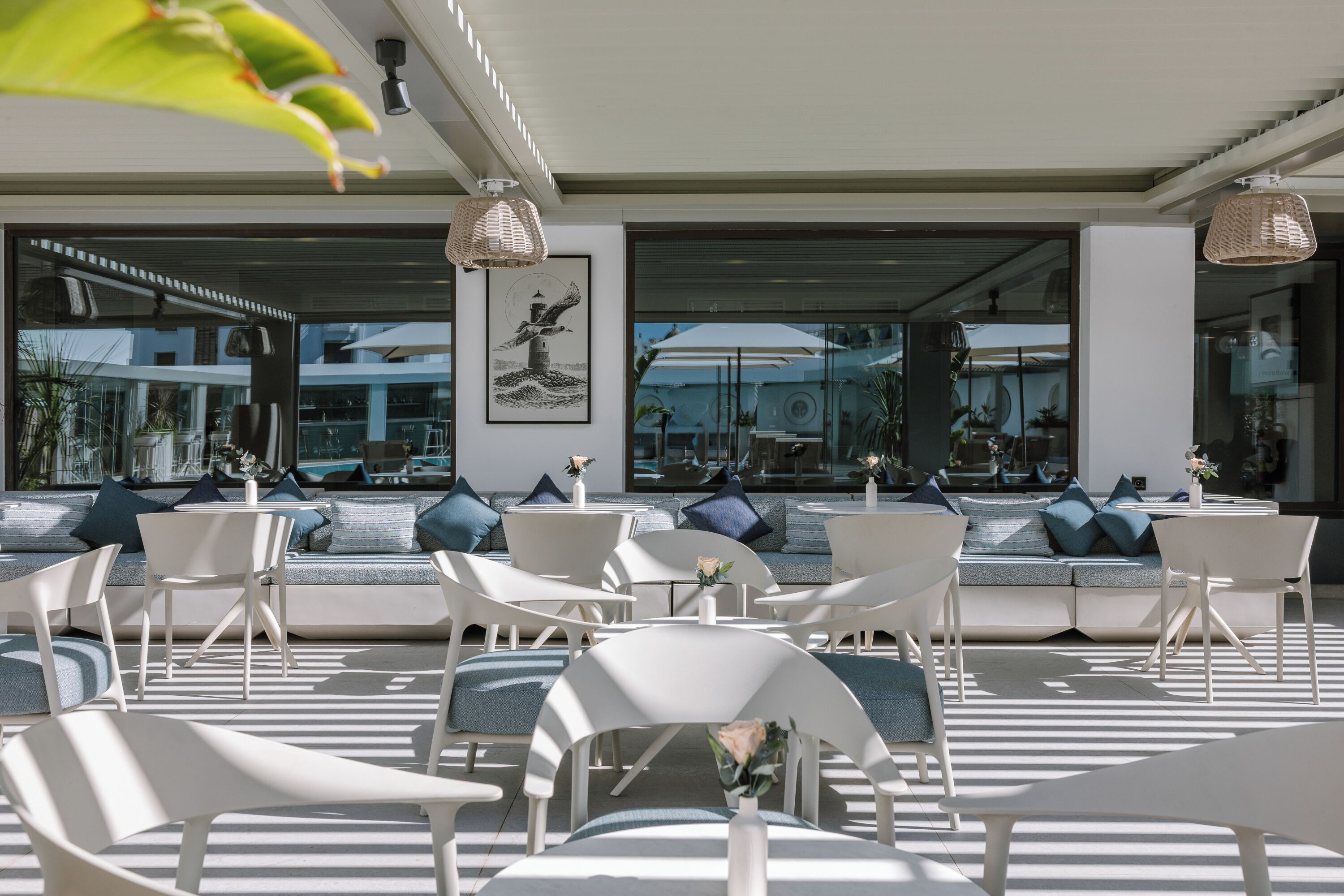 A modern outdoor seating area with white chairs and sofas, large windows, and a framed artwork on the wall.