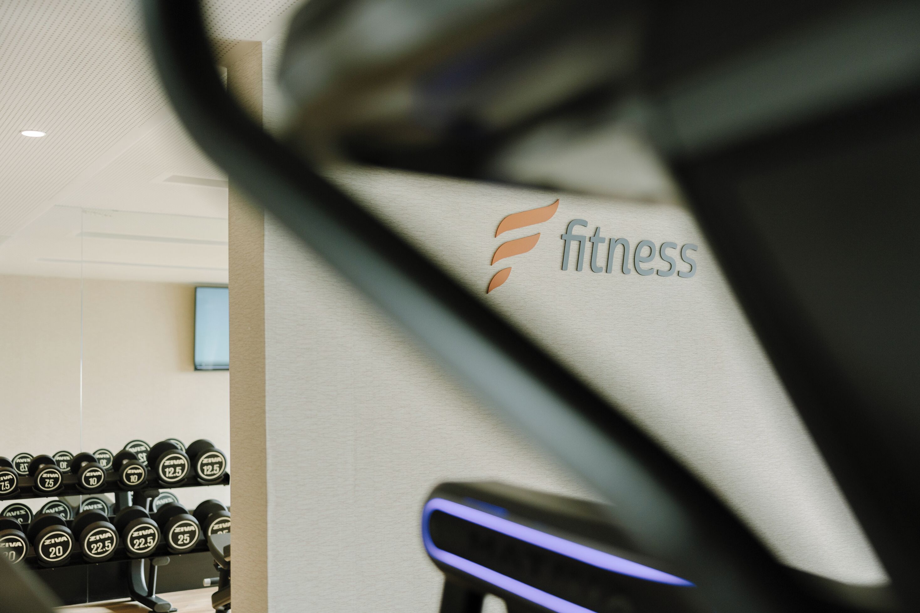 Une salle de sport avec un logo fixé au mur, une rangée d’haltères et un tapis de course.