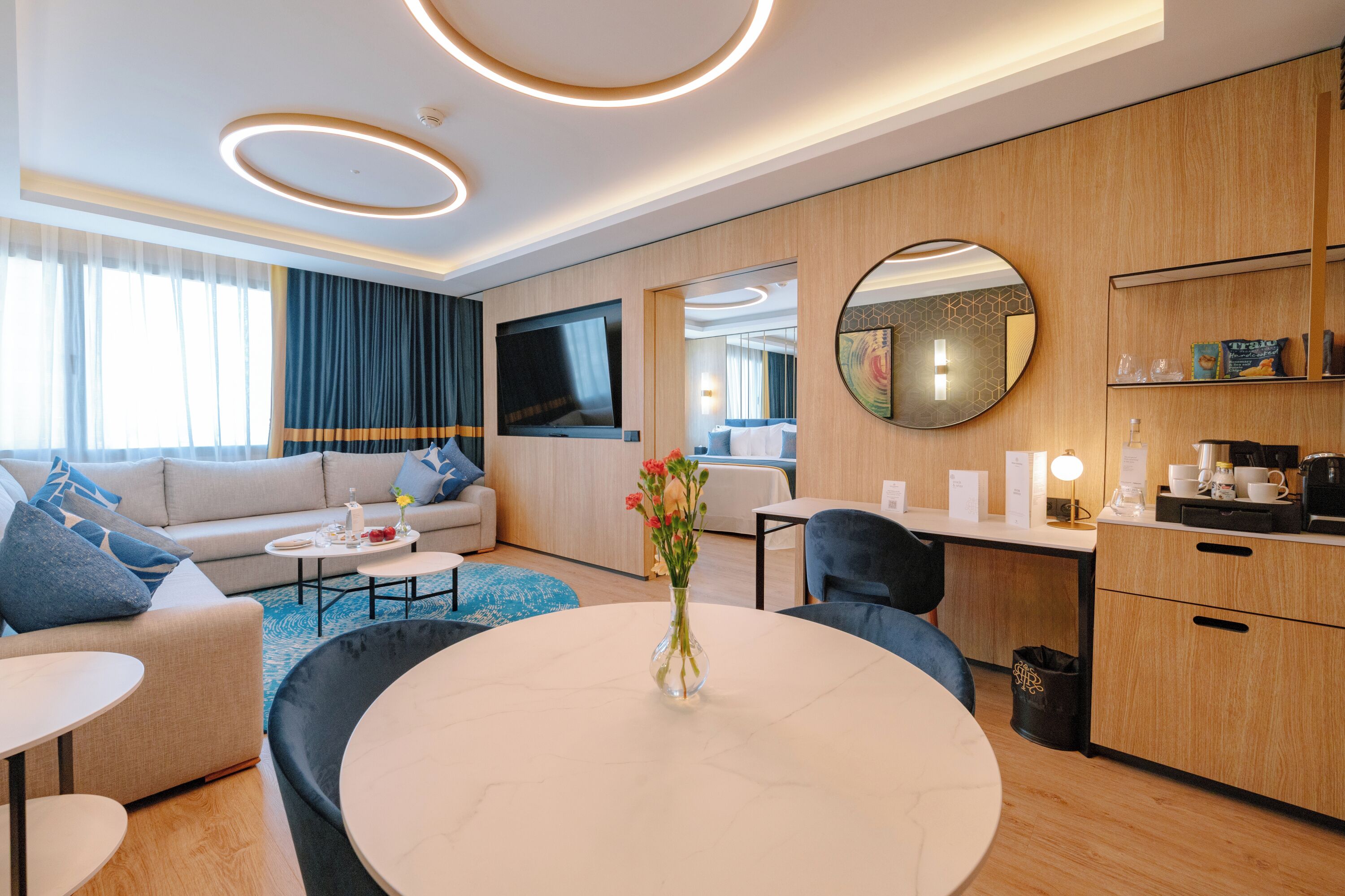 Una habitación de hotel moderna con sofá, mesa de comedor, área de cocina y un espejo grande.