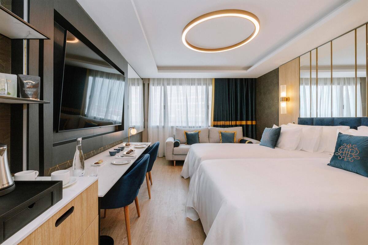 A hotel room with a large bed, a desk with a chair, a TV mounted on the wall, and a window with curtains.