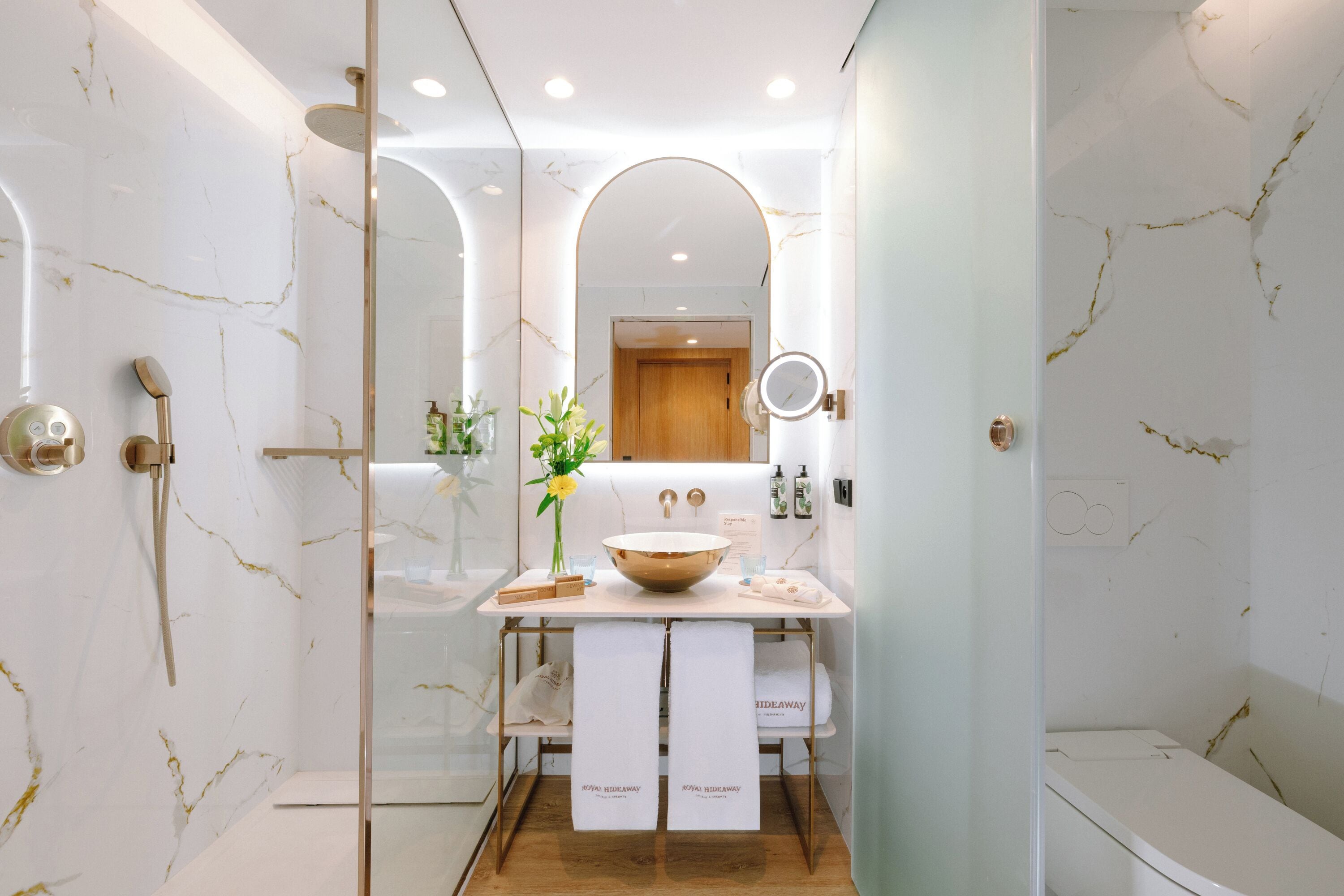 Une salle de bain moderne avec un mur en marbre, une douche à parois de verre, un lavabo en forme de vasque et un miroir.