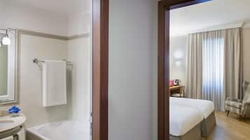Una habitación de hotel con baño, una cama, una silla y un escritorio.