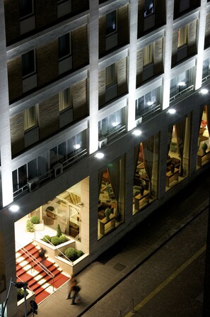 A multi-story hotel with a modern design, featuring balconies, large windows, and a central atrium with seating areas.