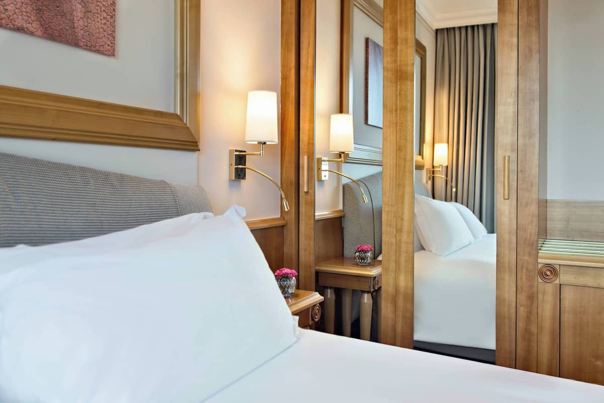 A hotel room with a bed, bedside tables, lamps, and a mirror.