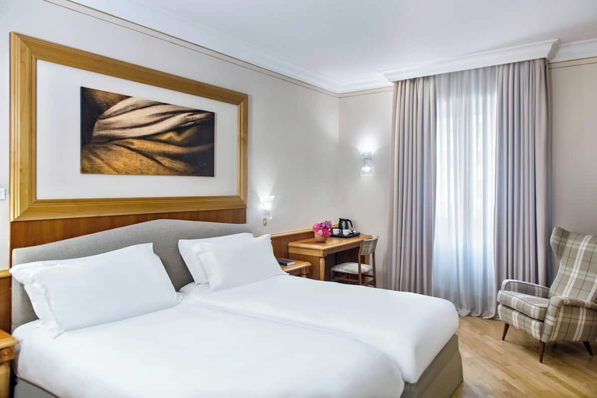 A hotel room with a large bed, a desk with a chair, a lamp, and a painting on the wall.