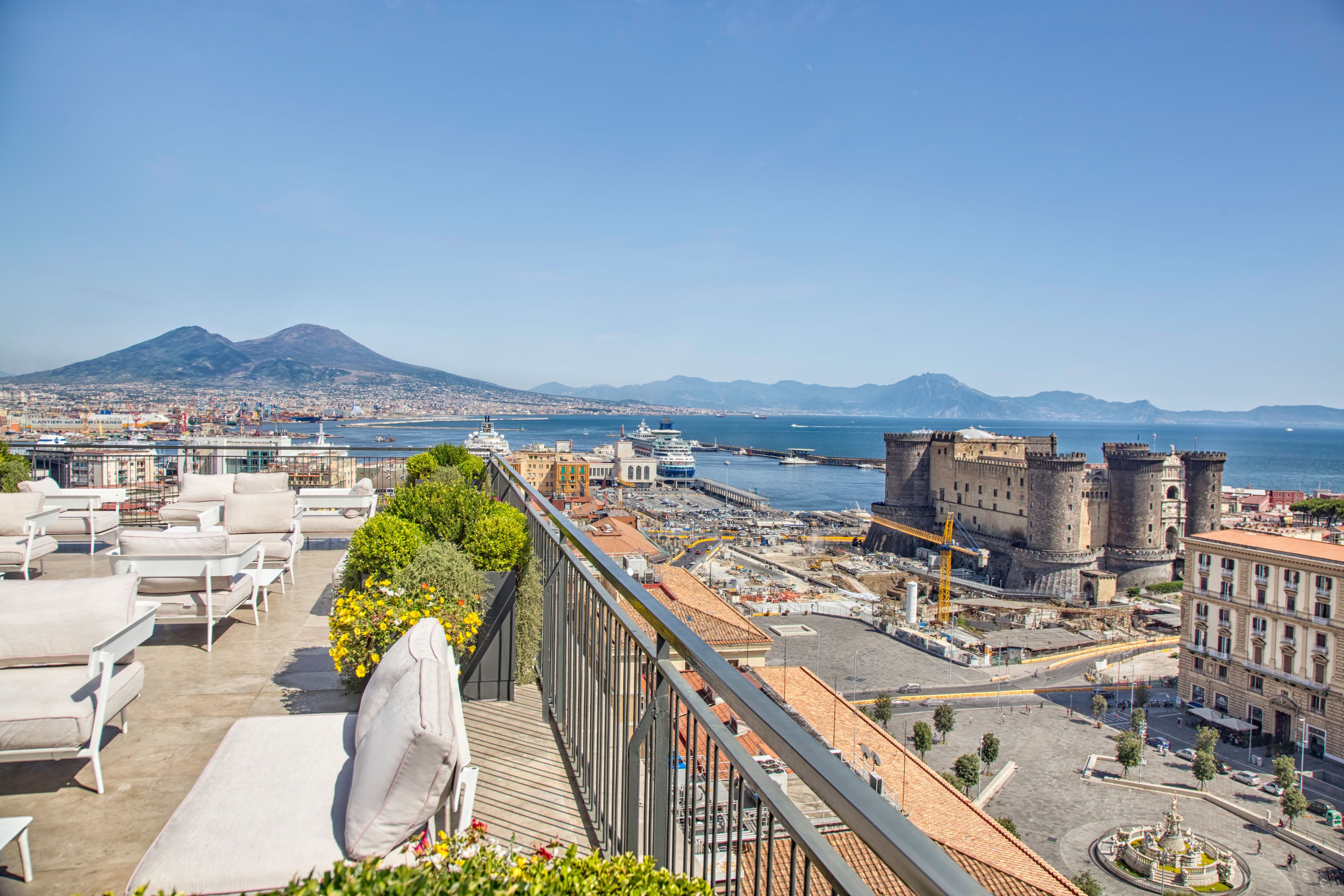 A rooftop terrace with lounge chairs, a view of the harbor, and a historic castle.