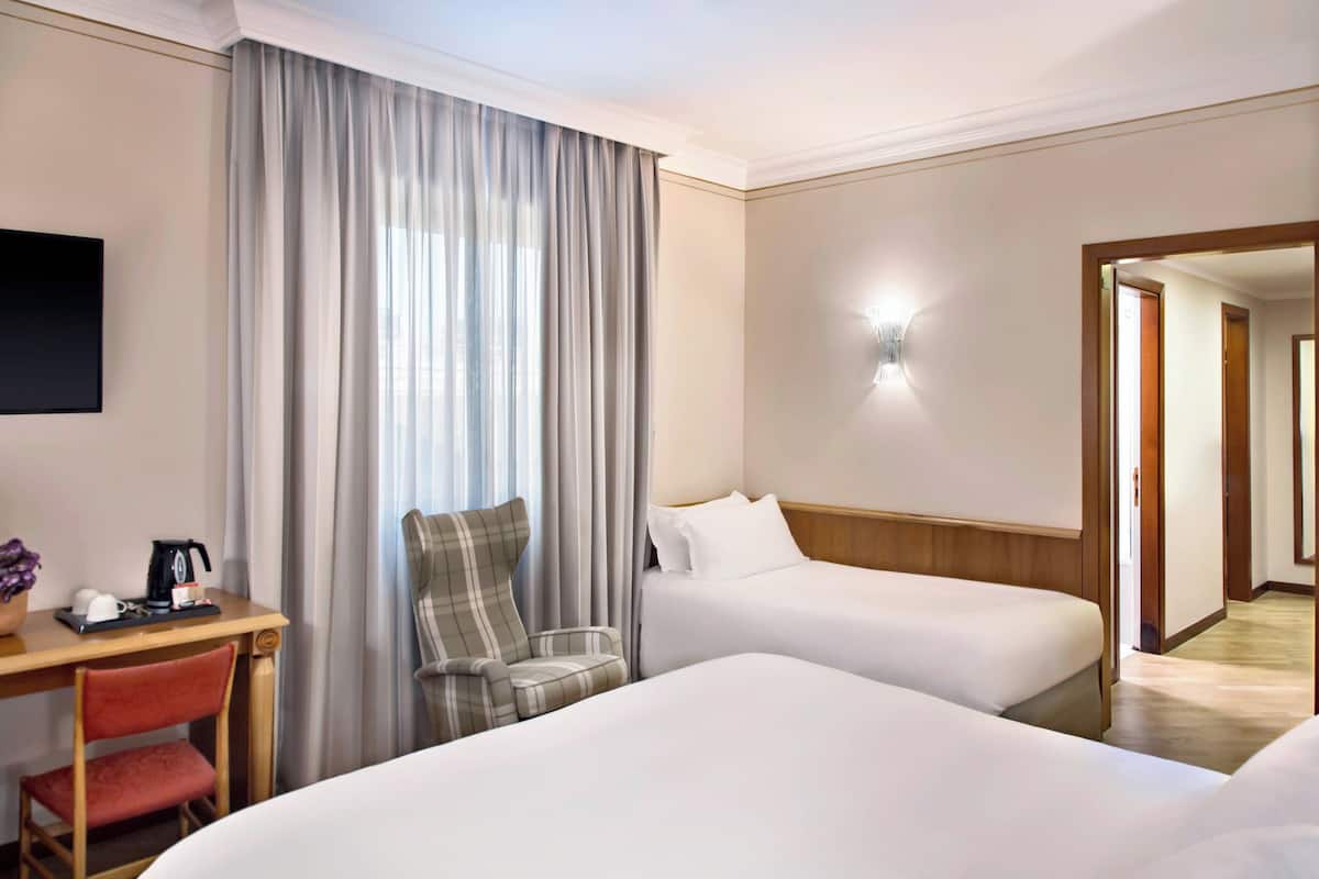 A hotel room with two beds, a desk with a coffee maker, a chair, and a TV.