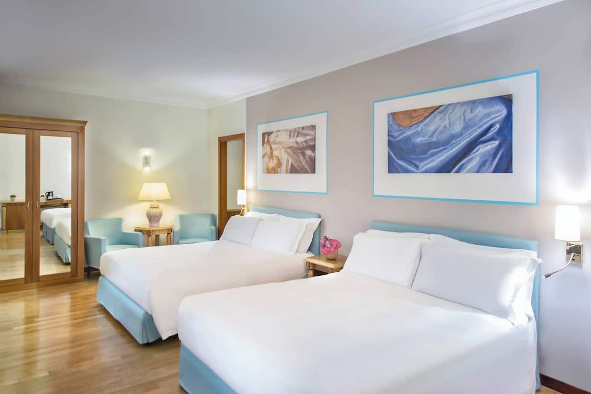 A hotel room with two beds, a mirror, a lamp, and artwork on the walls.