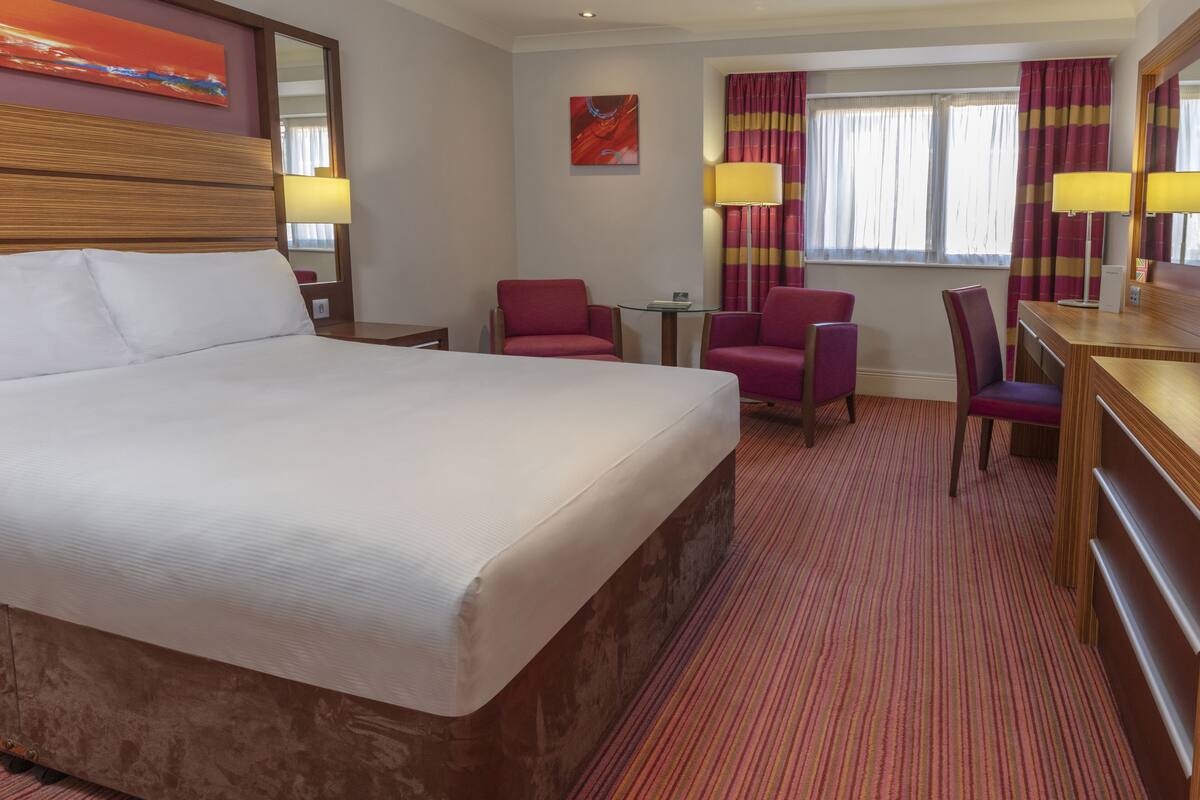 Une chambre d’hôtel avec un grand lit, deux fauteuils, un bureau et une petite table.
