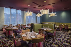 Un restaurant doté de nombreuses tables et de banquettes, de grandes fenêtres et d’un éclairage moderne.