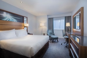 Une chambre d’hôtel avec un grand lit, un bureau, une chaise et un miroir.