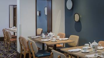 A hotel dining area with tables set for tea service, chairs with patterned cushions, and decorative wall mirrors.