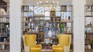 Een modern interieur met twee gele fauteuils, een houten boekenkast vol decoratieve objecten en een dakvenster erboven.