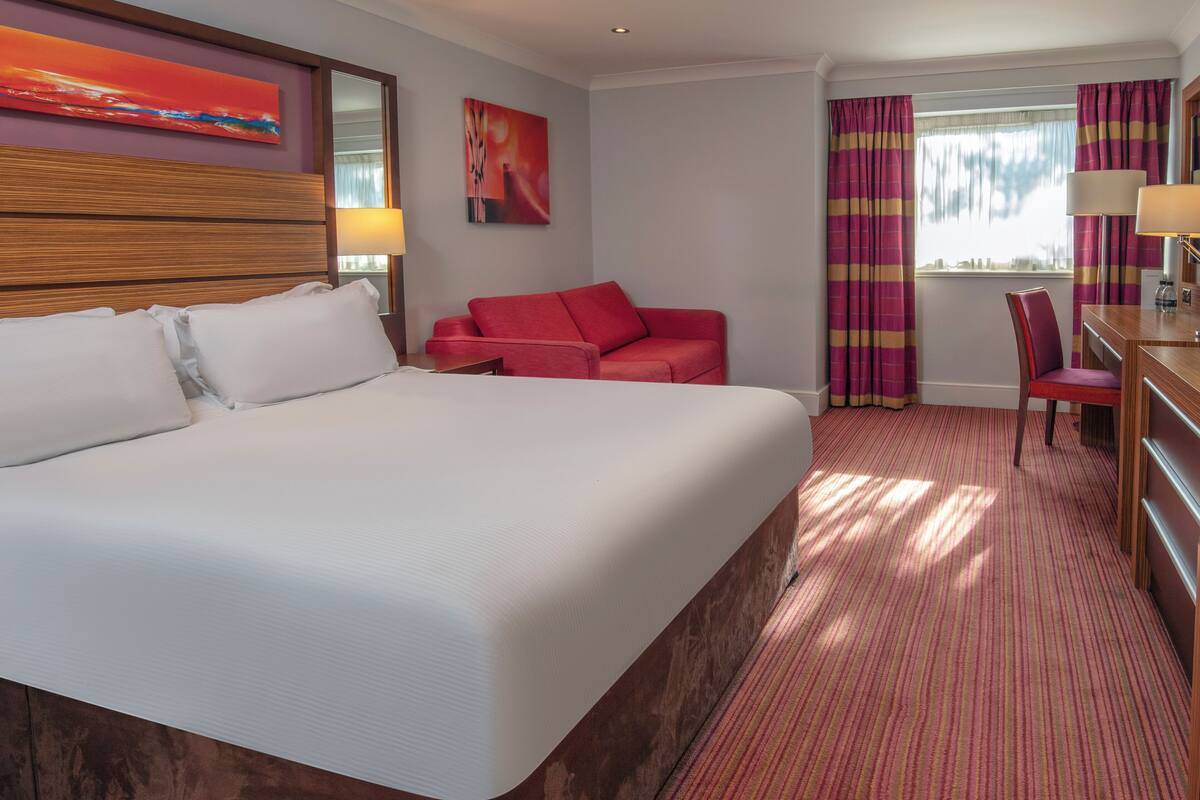 Une chambre d’hôtel avec un grand lit, un canapé rouge, un bureau et une chaise.
