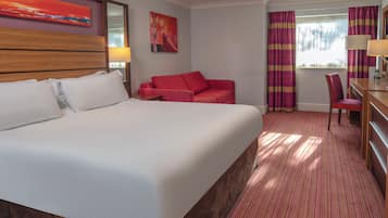 Una habitación de hotel con una cama grande, un sofá rojo, un escritorio y una silla.
