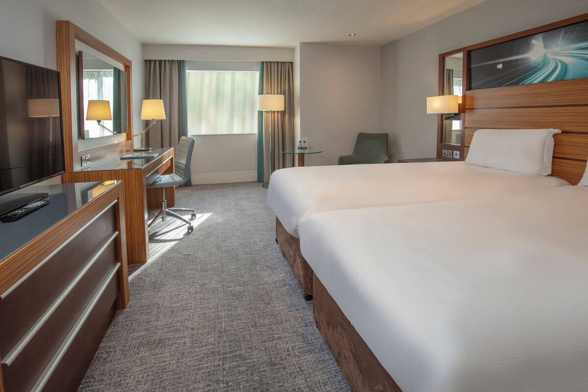 Une chambre d’hôtel avec un grand lit, un bureau avec une chaise, une télévision et une fenêtre avec des rideaux.