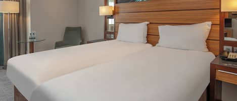 A hotel room with a large bed, bedside lamps, a chair, and a glass table.