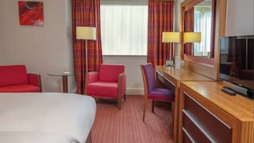 Une chambre d’hôtel comprenant un lit, un bureau avec une télévision, deux chaises, une petite table et une fenêtre avec des rideaux.