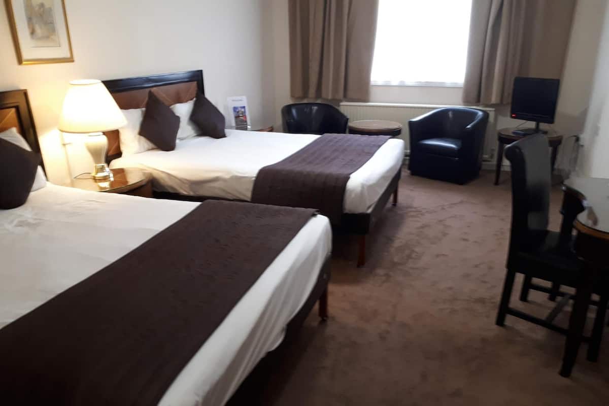 Habitación de hotel con dos camas, un escritorio, una silla, un televisor y una ventana con cortinas.