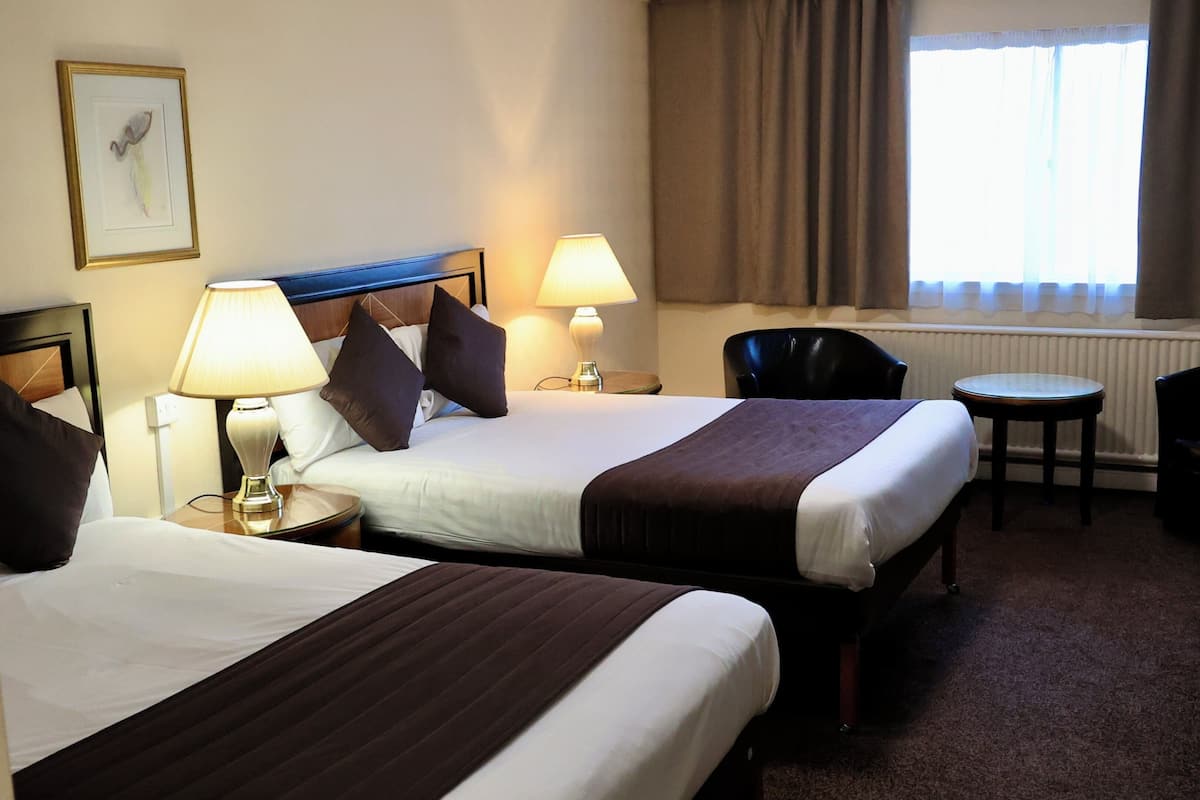 Habitación de hotel con dos camas, una silla, una mesita y una ventana con cortinas.