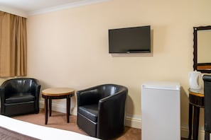 A hotel room with two black leather armchairs, a small round table, a flat-screen TV mounted on the wall, a white refrigerator, and a coffee maker on a side table. - Britannia Aberdeen Hotel (Aberdeen)