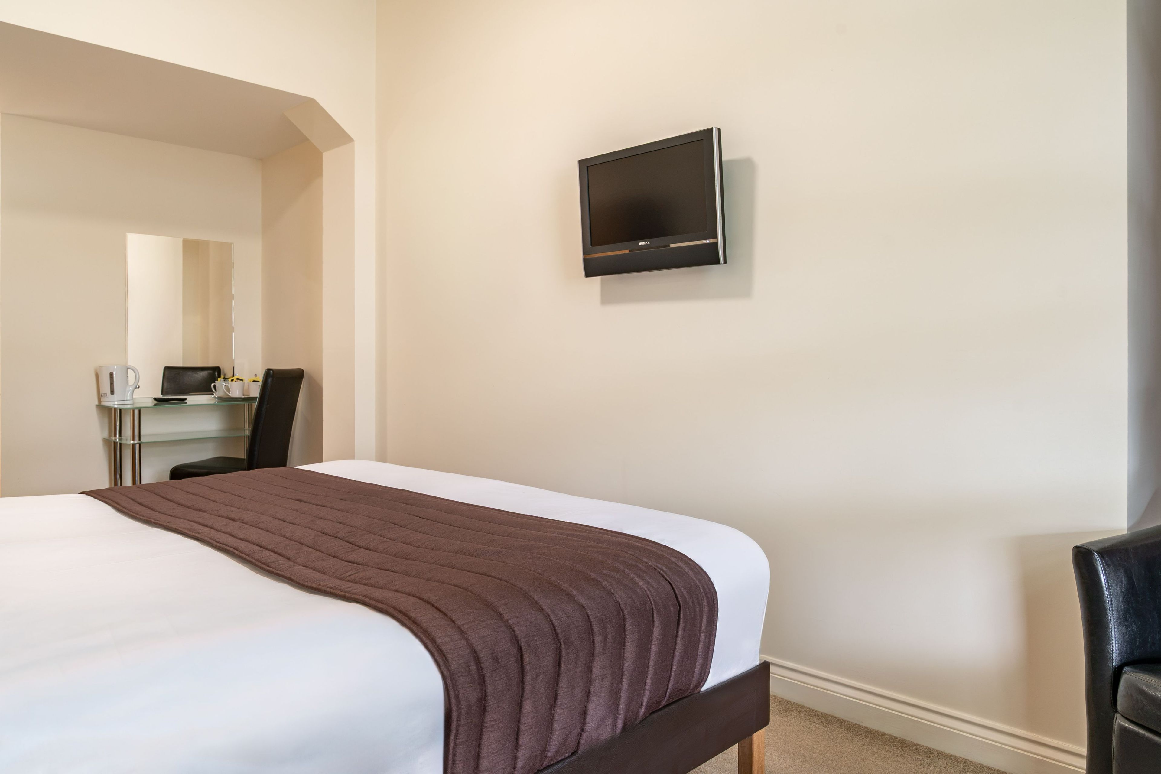 A hotel room with a bed, a desk, a chair, and a television mounted on the wall.