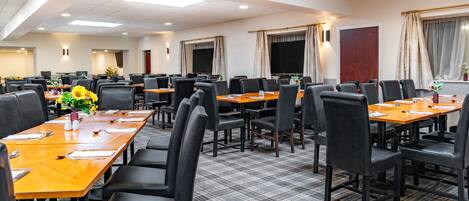 Une salle de conférence dotée de plusieurs tables et chaises, d’un grand écran et d’un sol recouvert de moquette.