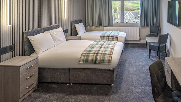 A hotel room with two beds, a desk, a chair, and a TV.