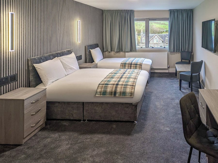 A hotel room with two beds, a desk, a chair, and a TV.
