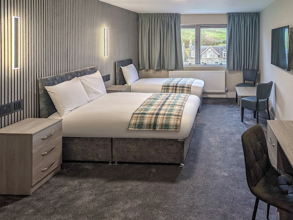 A hotel room with two beds, a desk, a chair, and a TV.