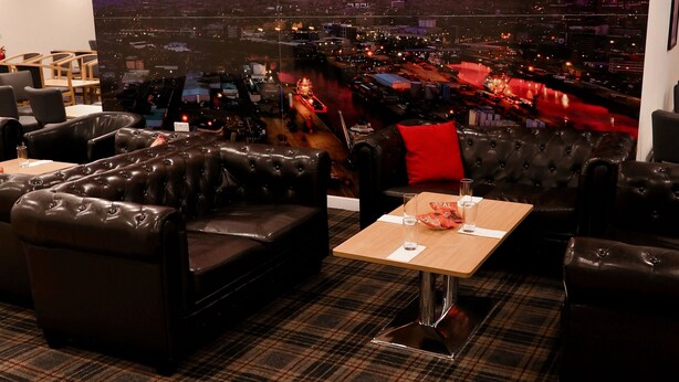 A lounge area with leather sofas and a table, a cityscape view through a large window, and a plaid carpet. - Britannia Aberdeen Hotel (Aberdeen)