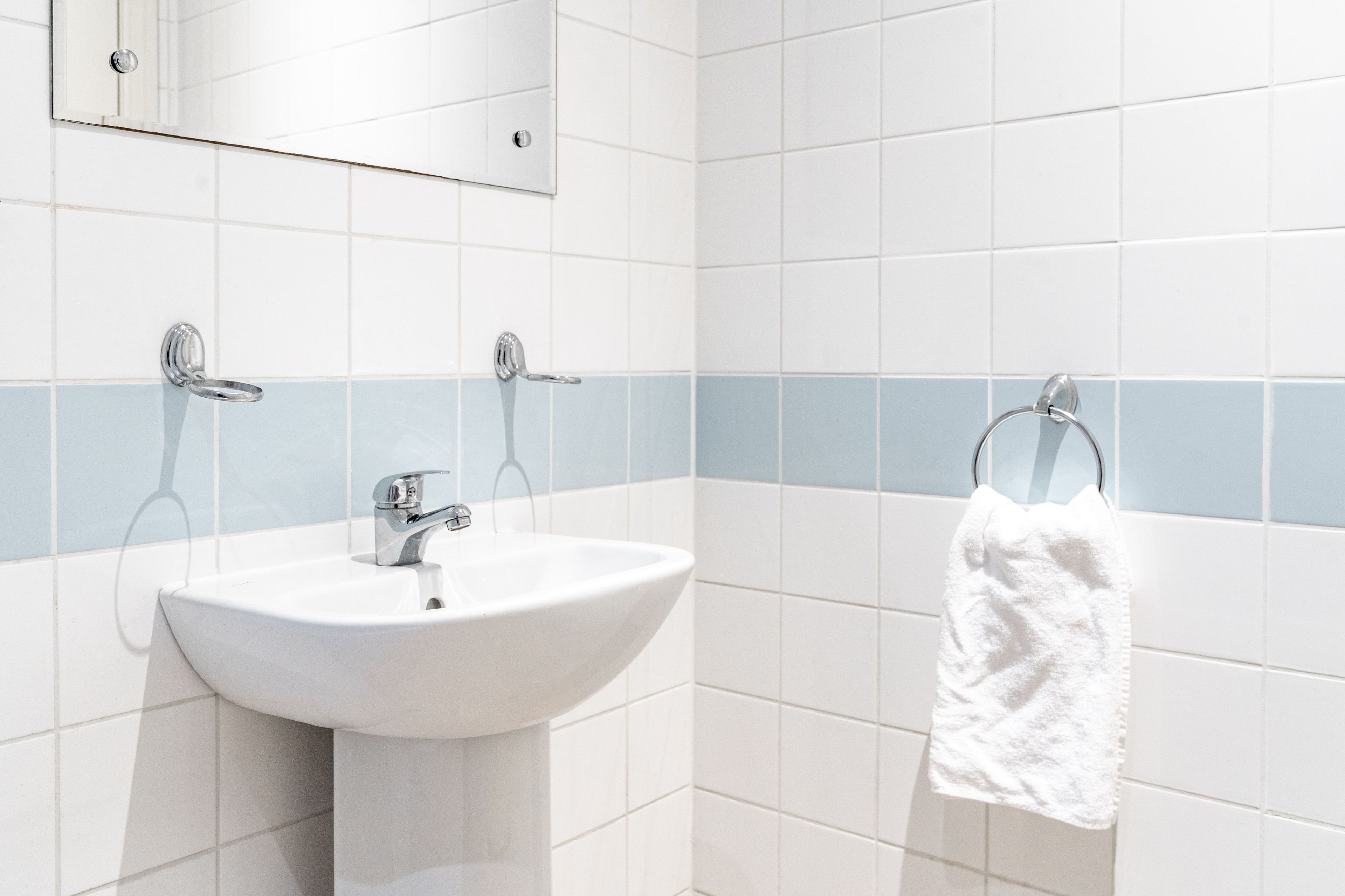 A bathroom with a white sink, a mirror, and a towel rack.