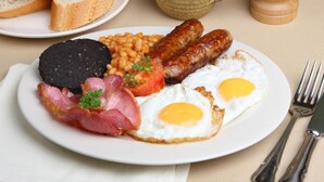 A plate of breakfast food including sausages, eggs, beans, and bacon.