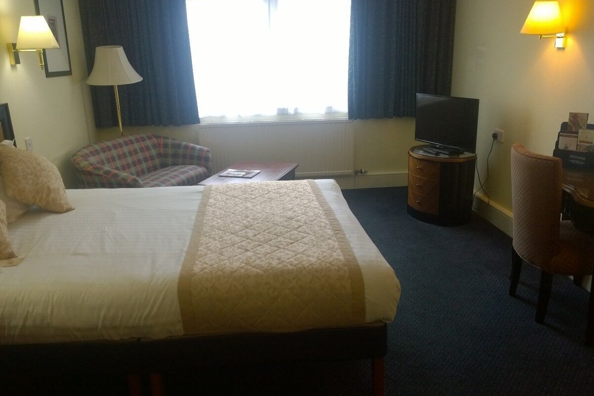 A hotel room with a bed, a desk, a chair, a television, and a lamp.