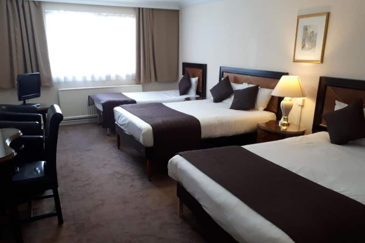 Habitación de hotel con tres camas, un escritorio y una silla.