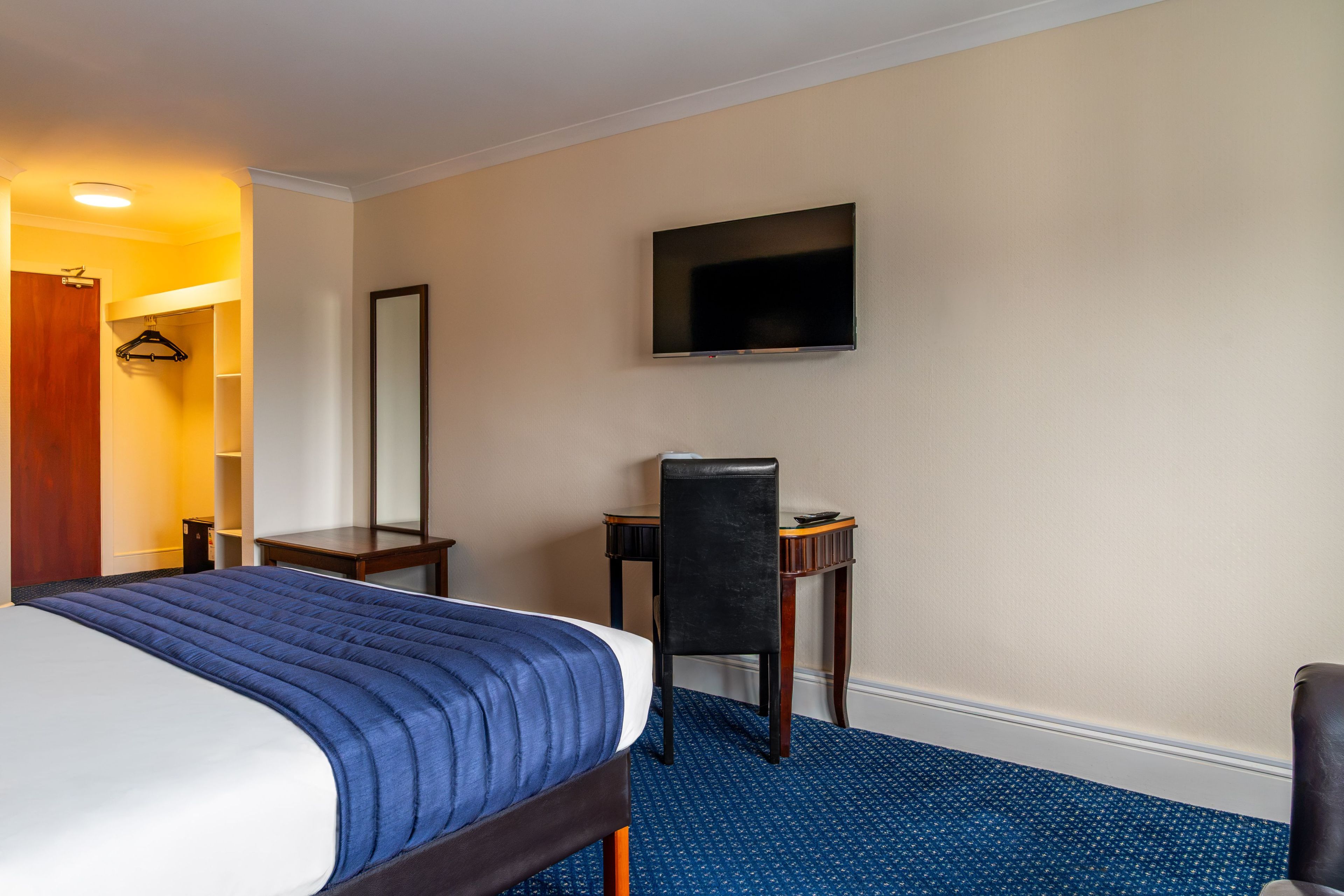 Una habitación de hotel con cama, escritorio, silla, televisor y armario.