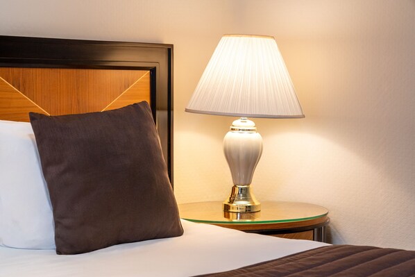 Una cama bien hecha con un cojín y una lámpara de noche sobre una mesita.