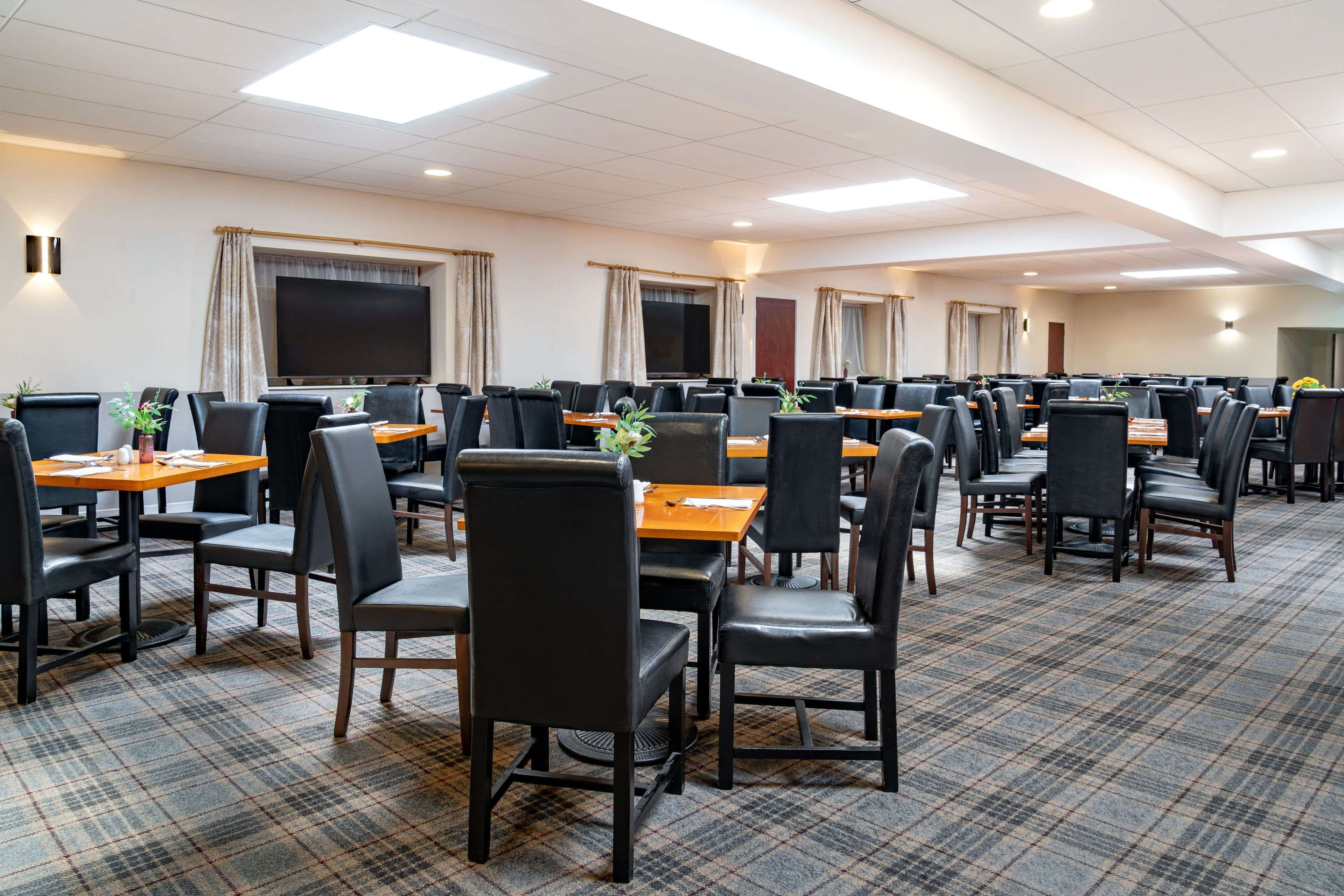 A conference room with multiple tables and chairs, equipped with screens and a large flat-screen TV.