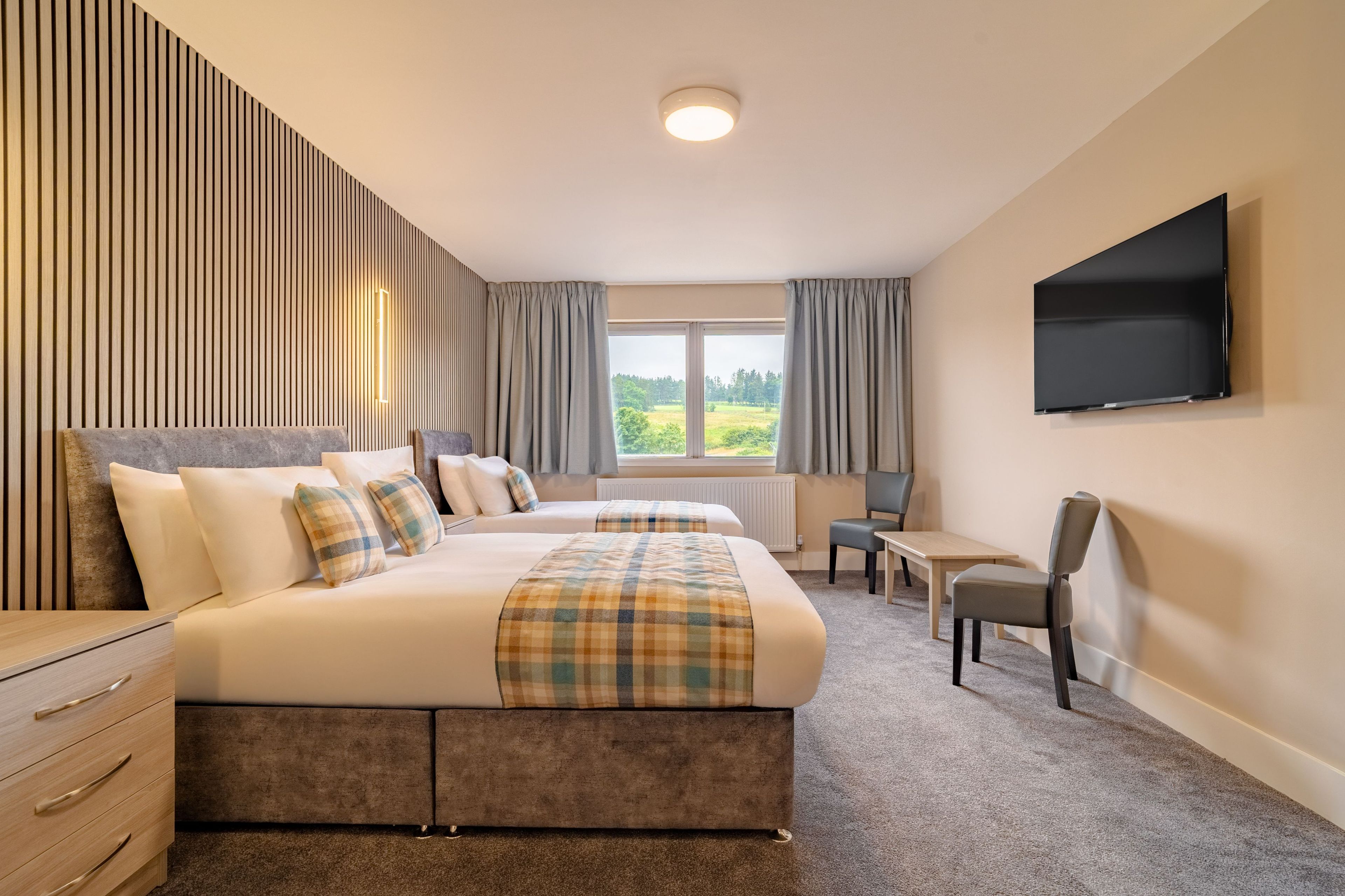 Une chambre d’hôtel avec un grand lit, un bureau, une chaise, une télévision et une fenêtre avec des rideaux.