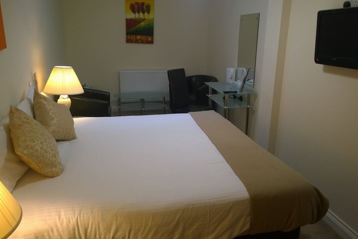 Habitación de hotel con cama, escritorio, silla, lámpara y televisor de pantalla plana.