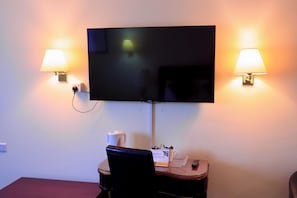 A hotel room with a flat-screen TV mounted on the wall, two bedside lamps, a small table with a coffee maker, and a chair. - Britannia Aberdeen Hotel (Aberdeen)
