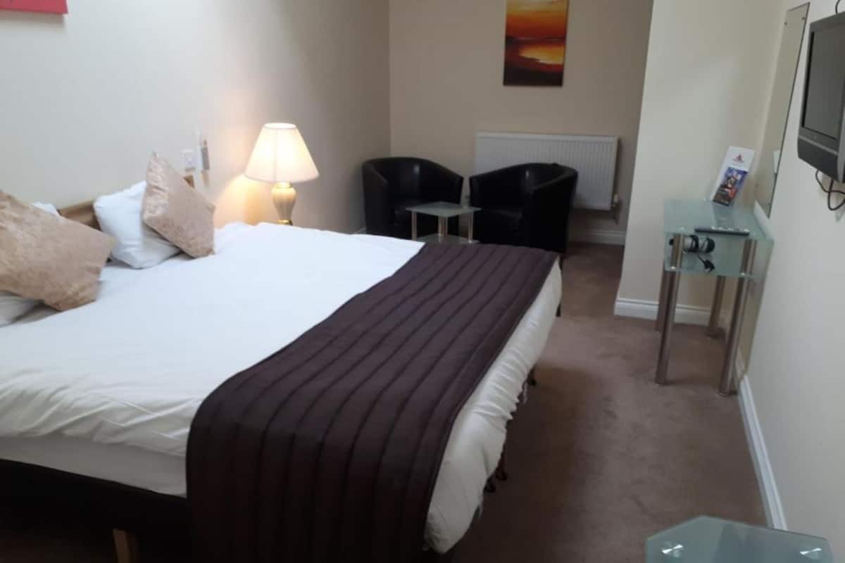 Una habitación de hotel con cama, escritorio, silla, lámpara y televisión.