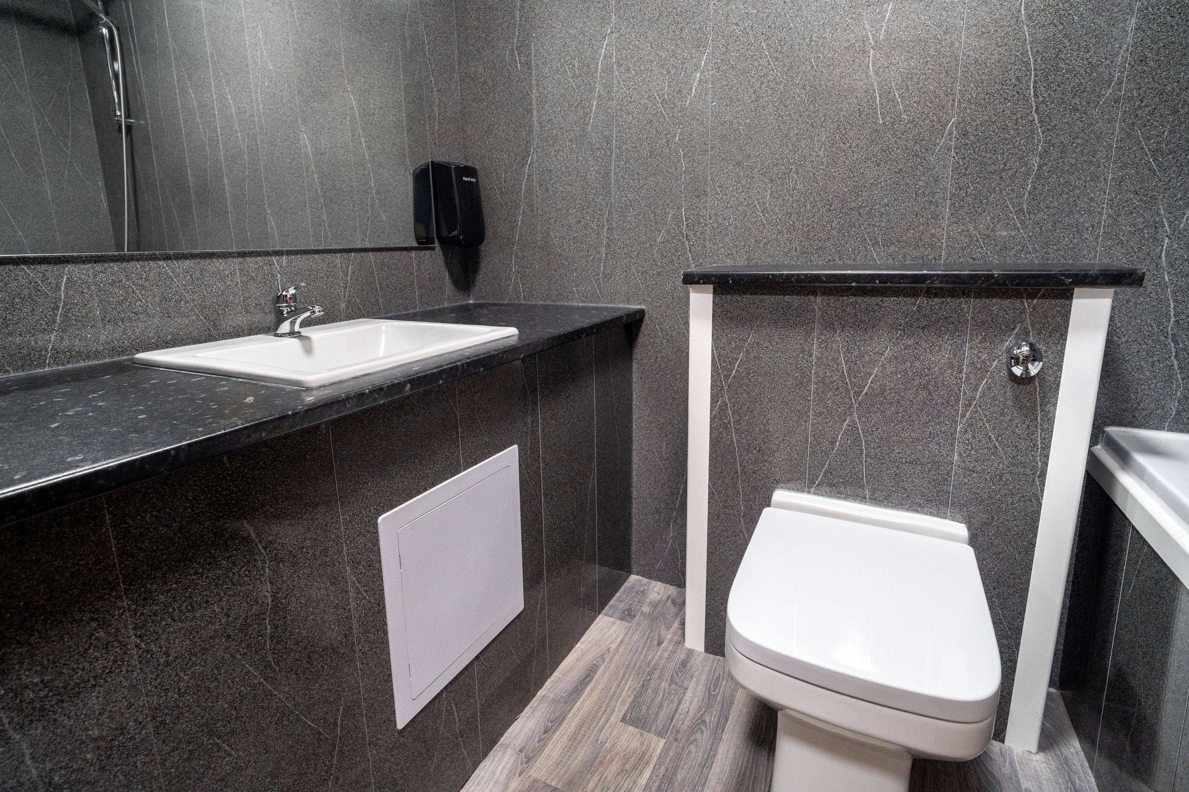 Une salle de bain moderne avec un plan de toilette en marbre foncé, un lavabo blanc et des toilettes.
