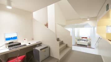 Un espacio de oficina moderno con escritorio, computadora, impresora y una escalera que conduce a una sala de estar con sofá y mesa de centro.