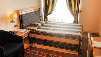 A hotel room with a bed, a desk with a telephone, a chair, and a nightstand.