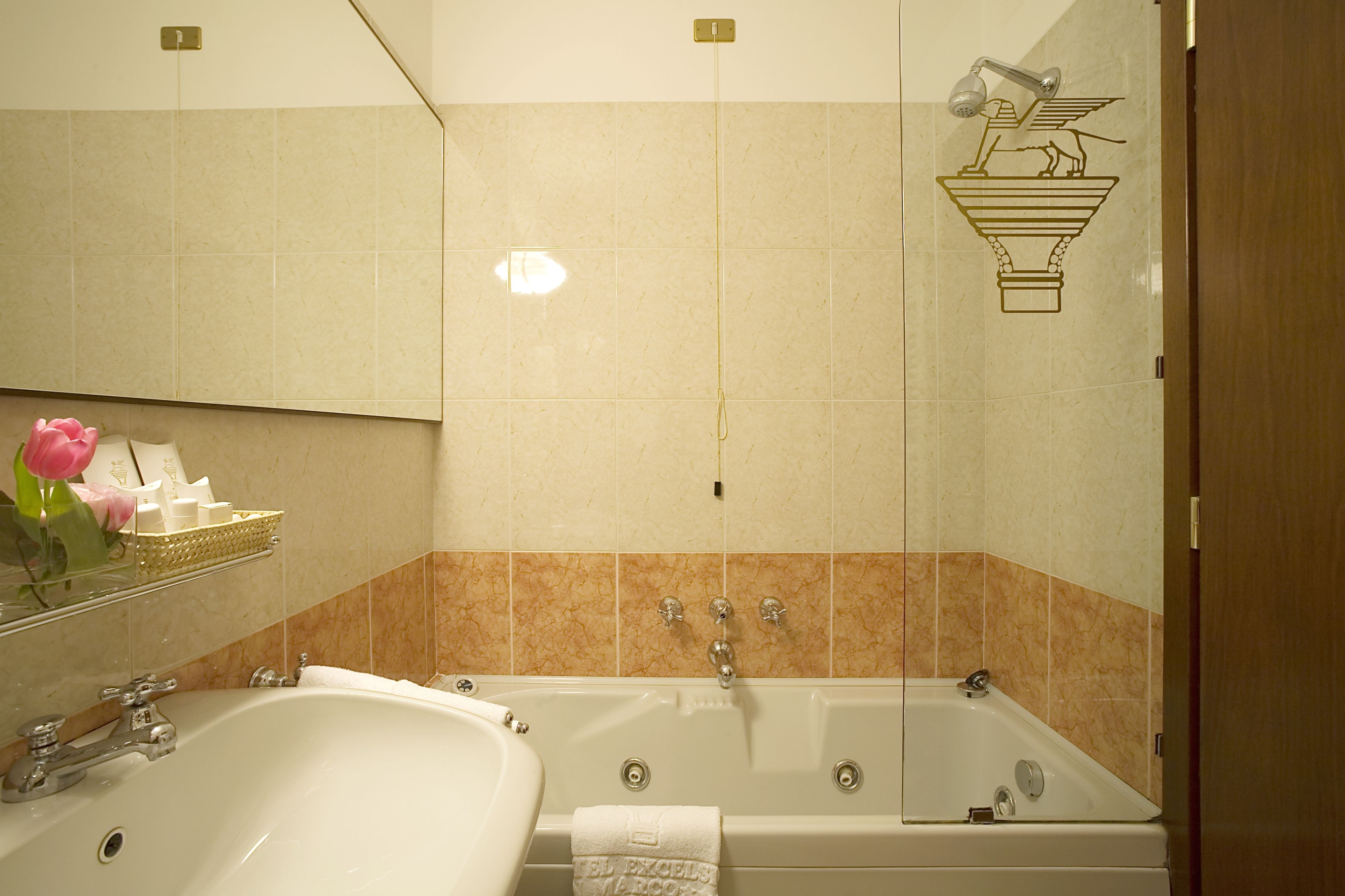 Une salle de bain avec une grande baignoire, un lavabo et un miroir. On y trouve un porte-serviettes avec une serviette et un vase avec des fleurs.