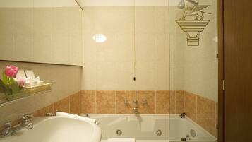 A bathroom with a large bathtub, a sink, and a mirror. There is a towel rack with a towel and a flower vase.