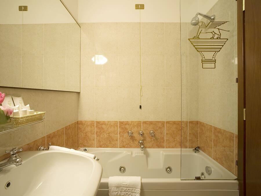 A bathroom with a large bathtub, a sink, and a mirror. There is a towel rack with a towel and a flower vase.